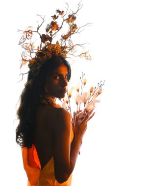 Arka planda, altın sarısı bir ışıkla parıldayan, çiçekli bir taç takan, elinde çiçekler tutan, yumuşak, ruhani bir fantezi tanrıçası fantezi karakterini anımsatan bir kadının siluet portresi.