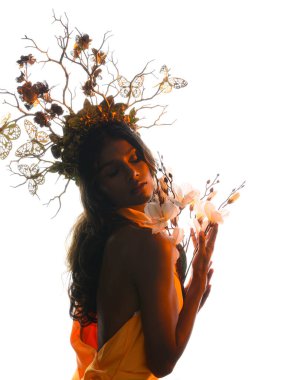 Arka planda, altın sarısı bir ışıkla parıldayan, çiçekli bir taç takan, elinde çiçekler tutan, yumuşak, ruhani bir fantezi tanrıçası fantezi karakterini anımsatan bir kadının siluet portresi.