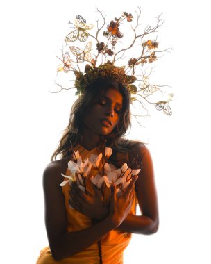 Arka planda, altın sarısı bir ışıkla parıldayan, çiçekli bir taç takan, elinde çiçekler tutan, yumuşak, ruhani bir fantezi tanrıçası fantezi karakterini anımsatan bir kadının siluet portresi.