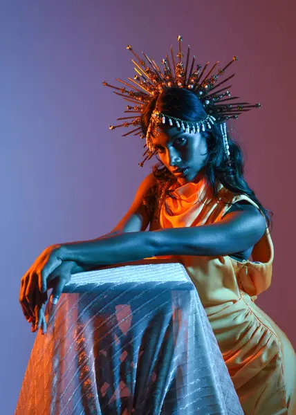 Güzel esmer bir kadının portresi. Fantezi tacını takıyor ve göz alıcı sarı bir balo elbisesi giyiyor. Sinematik renkli ışıklandırmayla stüdyonun arka planında zarif bir poz..