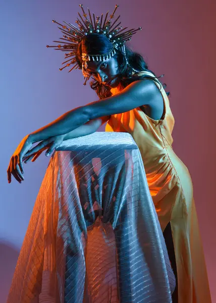 Güzel esmer bir kadının portresi. Fantezi tacını takıyor ve göz alıcı sarı bir balo elbisesi giyiyor. Sinematik renkli ışıklandırmayla stüdyonun arka planında zarif bir poz..