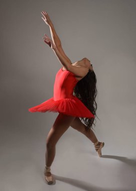 Kırmızı etekli esmer balerin ve sivri uçlu ayakkabılar, klasik dans pozlarında kameraya dönük bir şekilde duruyor, beyaz izole edilmiş stüdyo arka planında bale kostümü giyiyor..