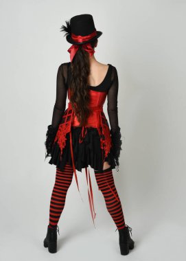 Uzun boylu, burlesk sirk sanatçısı, cadılar bayramı palyaço kostümlü, gotik şapkalı kadın model. Beyaz stüdyo arka planında izole edilmiş bir poz..