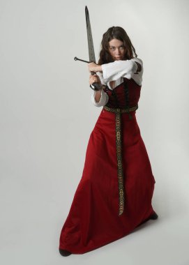 Fantezi kılıç tutan kırmızı ortaçağ tarihi bir elbise giyen güzel esmer kadın modelin portresi. Beyaz stüdyo arka planında izole bir figür..