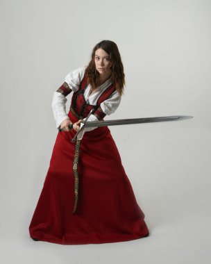 Fantezi kılıç tutan kırmızı ortaçağ tarihi bir elbise giyen güzel esmer kadın modelin portresi. Beyaz stüdyo arka planında izole bir figür..