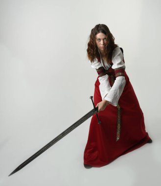 Fantezi kılıç tutan kırmızı ortaçağ tarihi bir elbise giyen güzel esmer kadın modelin portresi. Beyaz stüdyo arka planında izole bir figür..