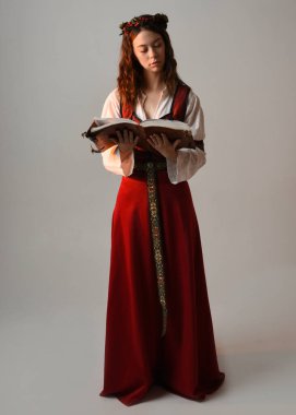 Kırmızı bir ortaçağ elbisesi giyen güzel esmer kadın model portresi, tarihi fantezi kostümü. Kitap tutuyor, poz veriyor. Stüdyo arka planında izole bir figür