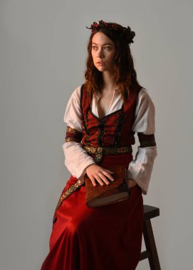 Kırmızı bir ortaçağ elbisesi giyen güzel esmer kadın model portresi, tarihi fantezi kostümü. Kitap tutuyor, poz veriyor. Stüdyo arka planında izole bir figür