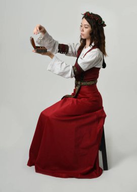 Kırmızı bir ortaçağ elbisesi giyen güzel, uzun boylu, esmer kadın model, tarihi fantezi kostüm. Elinde hazine mücevher kutusu tutuyordu. Stüdyo arka planında izole bir figür