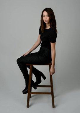 Siyah tişörtlü Esmer Kadın Yüksek Sandalye Stüdyosunun Yan Tarafında Beyaz Arkaplanda Oturan Modern Moda Pozu