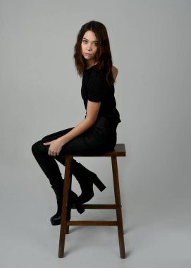 Siyah tişörtlü Esmer Kadın Yüksek Sandalye Stüdyosunun Yan Tarafında Beyaz Arkaplanda Oturan Modern Moda Pozu