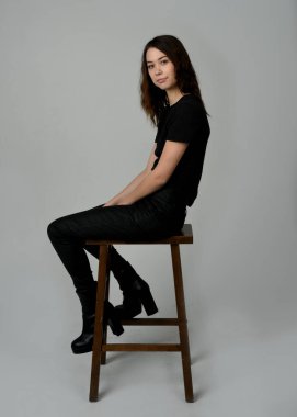 Siyah tişörtlü Esmer Kadın Yüksek Sandalye Stüdyosunun Yan Tarafında Beyaz Arkaplanda Oturan Modern Moda Pozu