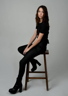 Siyah tişörtlü Esmer Kadın Yüksek Sandalye Stüdyosunun Yan Tarafında Beyaz Arkaplanda Oturan Modern Moda Pozu