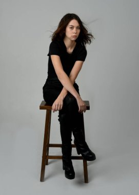 Siyah tişörtlü Esmer Kadın Yüksek Sandalye Stüdyosunun Yan Tarafında Beyaz Arkaplanda Oturan Modern Moda Pozu