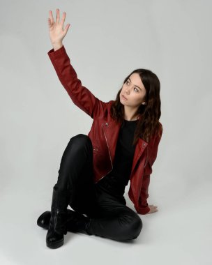 Kırmızı Deri Ceketli Esmer Kadın Diz çöküp Tam Uzunlukta Oturan Stüdyo Portresi Beyaz Arka planda İzole Edilen Modern Distopya Moda