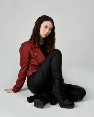 Kırmızı Deri Ceketli Esmer Kadın Diz çöküp Tam Uzunlukta Oturan Stüdyo Portresi Beyaz Arka planda İzole Edilen Modern Distopya Moda