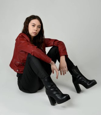 Kırmızı Deri Ceketli Esmer Kadın Diz çöküp Tam Uzunlukta Oturan Stüdyo Portresi Beyaz Arka planda İzole Edilen Modern Distopya Moda