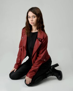 Kırmızı Deri Ceketli Esmer Kadın Diz çöküp Tam Uzunlukta Oturan Stüdyo Portresi Beyaz Arka planda İzole Edilen Modern Distopya Moda