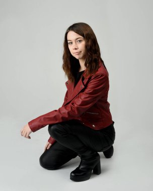 Kırmızı Deri Ceketli Esmer Kadın Diz çöküp Tam Uzunlukta Oturan Stüdyo Portresi Beyaz Arka planda İzole Edilen Modern Distopya Moda