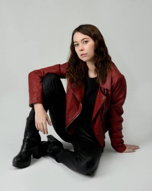 Kırmızı Deri Ceketli Esmer Kadın Diz çöküp Tam Uzunlukta Oturan Stüdyo Portresi Beyaz Arka planda İzole Edilen Modern Distopya Moda