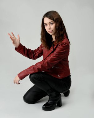 Kırmızı Deri Ceketli Esmer Kadın Diz çöküp Tam Uzunlukta Oturan Stüdyo Portresi Beyaz Arka planda İzole Edilen Modern Distopya Moda