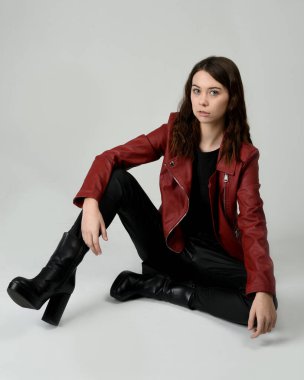 Kırmızı Deri Ceketli Esmer Kadın Diz çöküp Tam Uzunlukta Oturan Stüdyo Portresi Beyaz Arka planda İzole Edilen Modern Distopya Moda