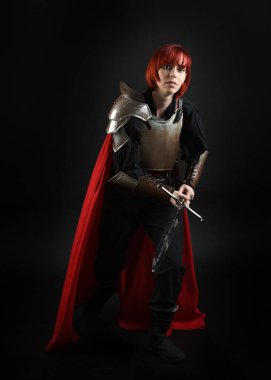 Tarihsel ortaçağ zırhlı fantezi savaşçı kadın modeli, kırmızı peri masalı pelerini, güçlü bir fantezi şövalyesinin kılıç tutan sinematik portresi. Destansı duruş, karanlık stüdyo arkaplan