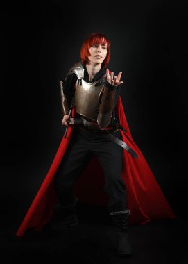 Tarihsel ortaçağ zırhlı fantezi savaşçı kadın modeli, kırmızı peri masalı pelerini, güçlü bir fantezi şövalyesinin kılıç tutan sinematik portresi. Destansı duruş, karanlık stüdyo arkaplan