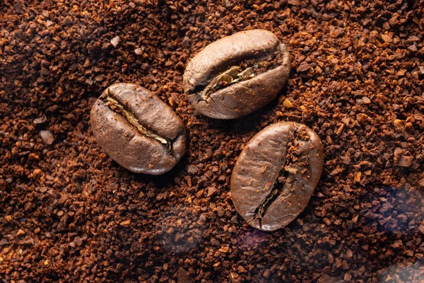 Three coffee beans lie on ground coffee close-up, roasted and ground coffee in light smoke.