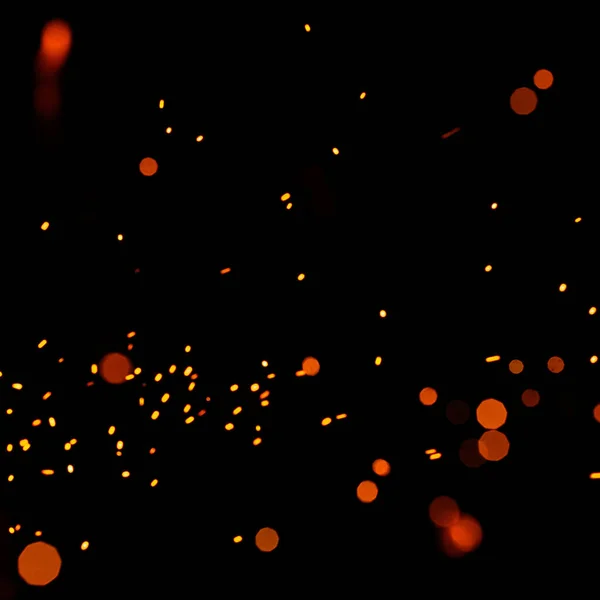 Bright yellow sparks on a black background, yellow bright round bokeh. Particles of burning embers fly and glow isolated in the night sky.