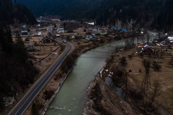 Top view of a mountain village of Ukraine in winter, a wide mountain river near the road.