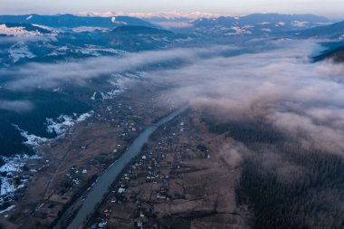 Ukrayna 'nın bir dağ köyünün kışın en üst manzarası, yol kenarında geniş bir dağ nehri..