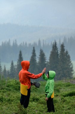 Vorokhta, Ukrayna 12 Haziran 2022: Parlak elbiseli turistler Karpatlar 'da dinleniyor, sis altındaki dağların arka planında iki çocuk.