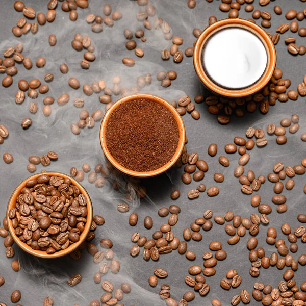 コーヒー豆 コーヒー豆 地面と準備ができた飲み物 暗い背景にコーヒー豆をこぼした3つのカップ — ストック写真