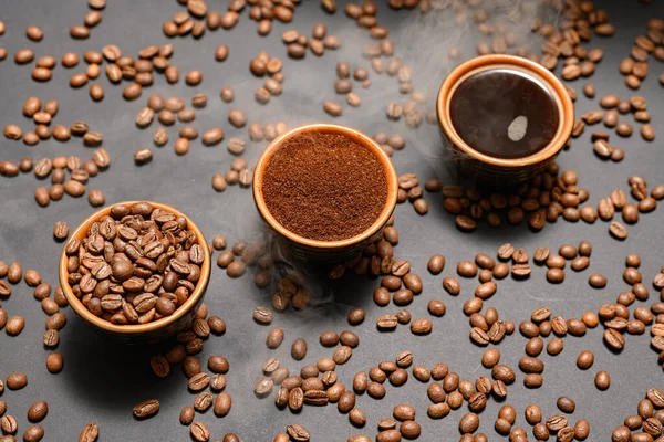 コーヒー豆 コーヒー豆 地面と準備ができた飲み物 暗い背景にコーヒー豆をこぼした3つのカップ — ストック写真