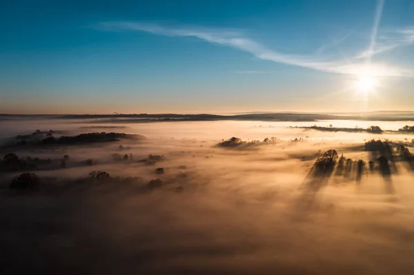 Flying over a village at dawn, bright sun on the horizon and fog over a small village, thick clouds and fog and a clear sky.