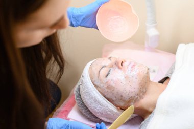 A client's visit to a cosmetologist, facial moisturizing with a cosmetic mask, a cosmetologist applies a mask to the face.