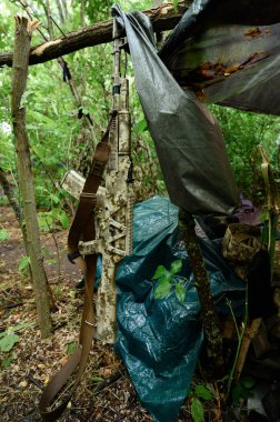Ormandaki çadırın yanında otomatik bir tüfek, Ukrayna 'daki savaş sırasında ormanda askeri bir çadır, savaşta olan bir askerin yaşam koşulları..