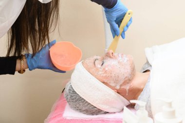 A client's visit to a cosmetologist, facial moisturizing with a cosmetic mask, a cosmetologist applies a mask to the face.