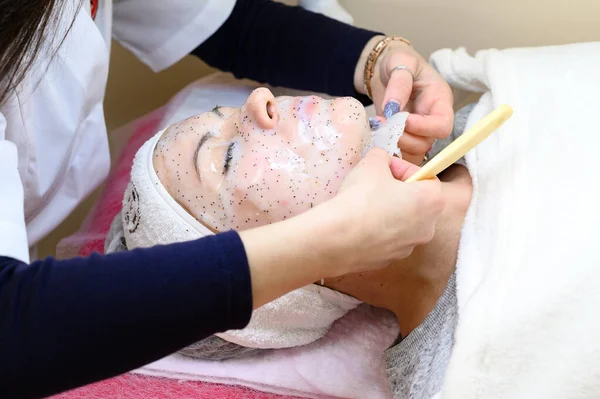 A beautician removes a moisturizing sheet mask on a woman\'s face with a spatula, cosmetology procedures.