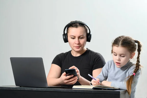 a young woman in headphones works on a laptop and at the same time exercises with her daughter, mother and daughter interaction.