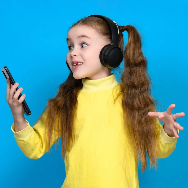Portret Dziewczynki Telefonem Słuchawkami Bezprzewodowymi Dziecka Żółtym Swetrze Niebieskim Tle — Zdjęcie stockowe