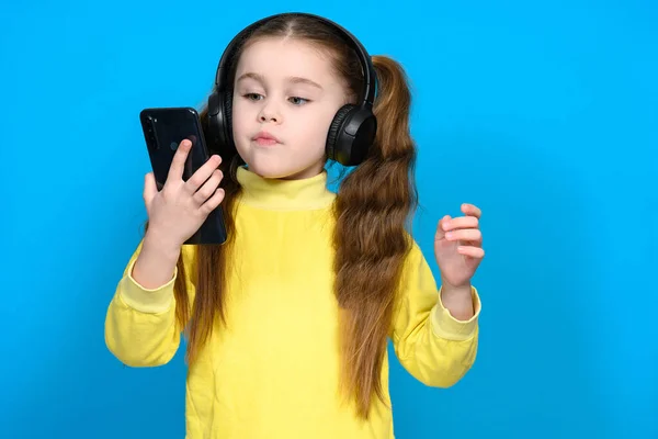 Portret Dziewczynki Telefonem Słuchawkami Bezprzewodowymi Dziecko Żółtym Swetrze Niebieskim Tle — Zdjęcie stockowe