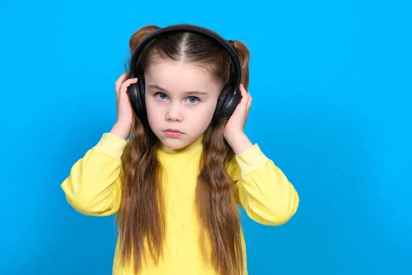 Dziewczyna Niebieskim Tle Żółtym Swetrze Słuchawkami Głowie Bezprzewodowe Słuchawki Dziecka — Zdjęcie stockowe