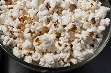 Siyah zemin üzerinde cam ve şeffaf patlamış mısır kasesi, kopyalama alanı ve metin için boş yer.