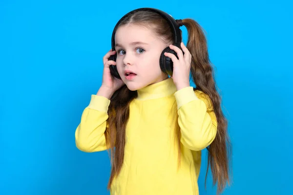 Mała Dziewczynka Żółtym Swetrze Niebieskim Tle Słucha Muzyki Słuchawkach Bezprzewodowych — Zdjęcie stockowe