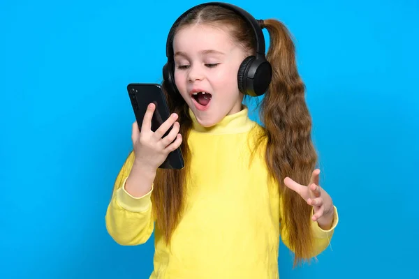 Portret Dziewczynki Telefonem Słuchawkami Bezprzewodowymi Dziecka Żółtym Swetrze Niebieskim Tle — Zdjęcie stockowe
