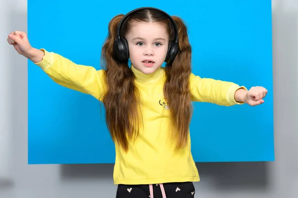 Happy Little Girl Bezprzewodowymi Słuchawkami Niebieskim Tle Robi Ruchy Taneczne — Zdjęcie stockowe