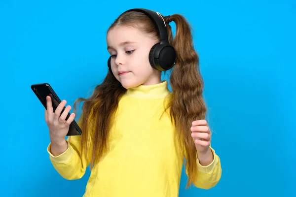 Portret Dziewczynki Telefonem Słuchawkami Bezprzewodowymi Dziecko Żółtym Swetrze Niebieskim Tle — Zdjęcie stockowe