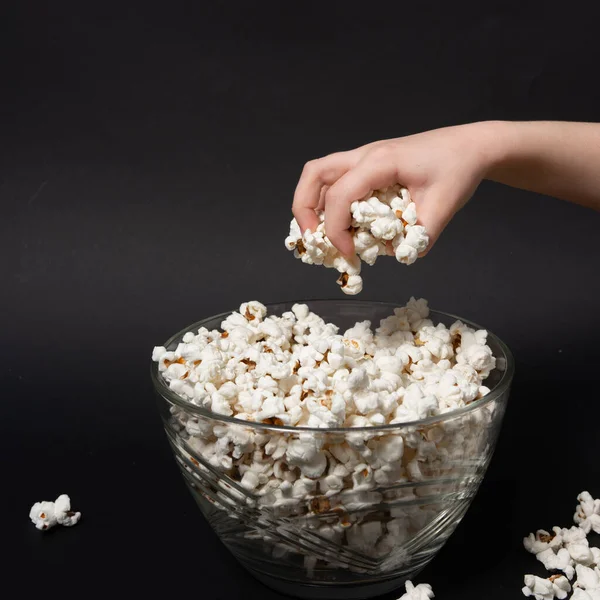 stock image A child's hand reaches for popcorn, which is in a glass bowl, copy space and popcorn on a black background.